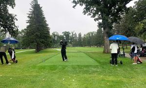 A golfer drives during the tournament. Spectators hold umbrellas.