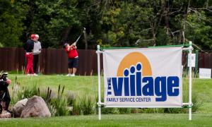 The Village banner is in the foreground while a golfer swings his club