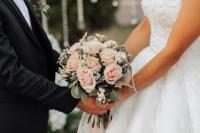 A groom (left) and a bride (right) both holding onto a pink bouquet of flowers